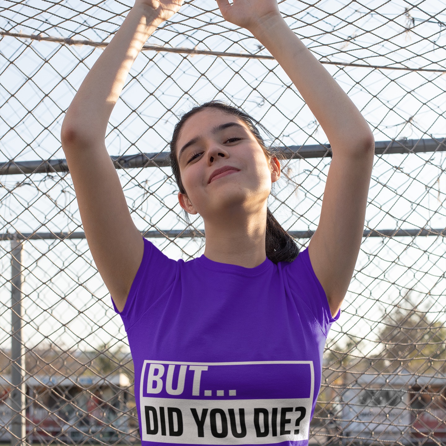 Person wearing a purple shirt with text in front of a chain-link fence.